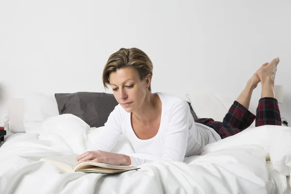 Kobieta czytająca książkę w łóżku — Zdjęcie stockowe