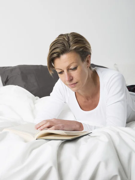 Frau liest Buch im Bett — Stockfoto