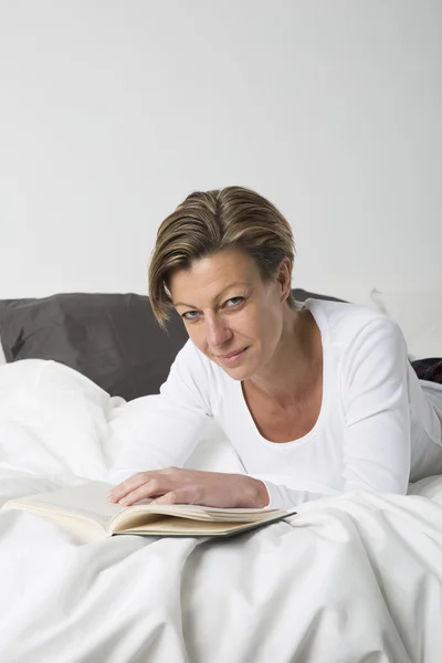 Lächelnde Frau beim Lesen eines Buches im Bett — Stockfoto