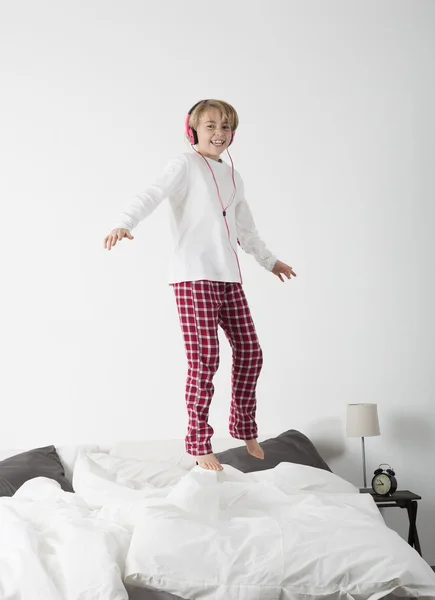 Kleines Mädchen mit Kopfhörern springt im Bett — Stockfoto