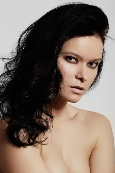 Schönes Frauenmodel mit perfekter dunkler Frisur, natürlichem Augen-Make-up und blassen Lippen, saubere Haut auf grauem Hintergrund lizenzfreie Stockbilder