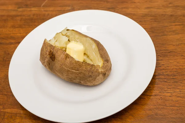 Καυτό βουτυρωμένο πατάτας στο άσπρο πιάτο και τραπέζι από ξύλο — Φωτογραφία Αρχείου