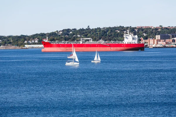 Witte zeilboten door oranje vrachtschip — Stockfoto