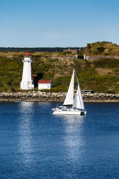 Білий вітрильник проходить білий маяк у сині води — стокове фото