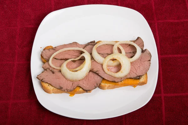 Soğan halkaları üzerinde kırmızı masa ile sıcak dilimlenmiş etli sandviç — Stok fotoğraf