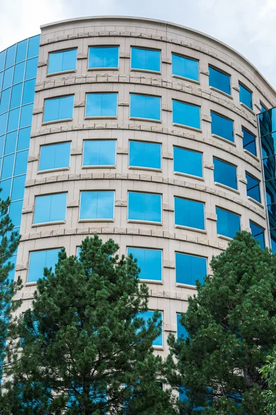 Ronde gebouw met blauw glas en pine bomen — Stockfoto