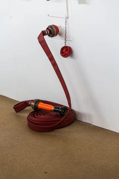 Roter Feuerwehrschlauch durch weißes Schott — Stockfoto