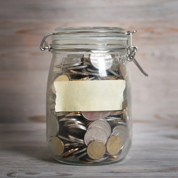 Coins in glass money jar with blank label — Stock Photo, Image