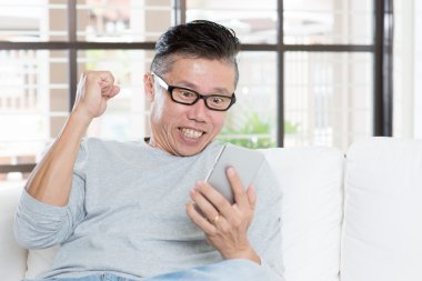 Mature Asian man celebrates success while using smartphone