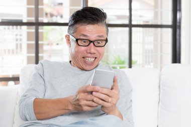 Mature Asian man getting excited while using smartphone