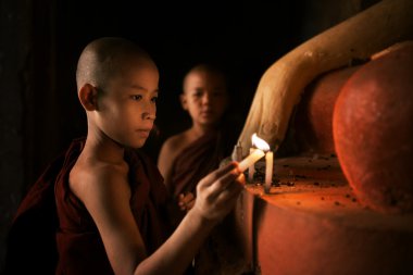 Buddhist novices praying with candlelight in monastery  clipart