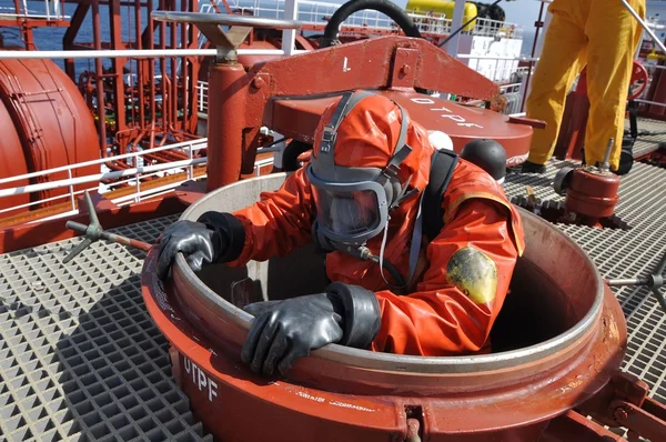 Hombre en traje químico que entra dentro del tanque de carga en el petrolero químico para la operación de limpieza Imagen de archivo