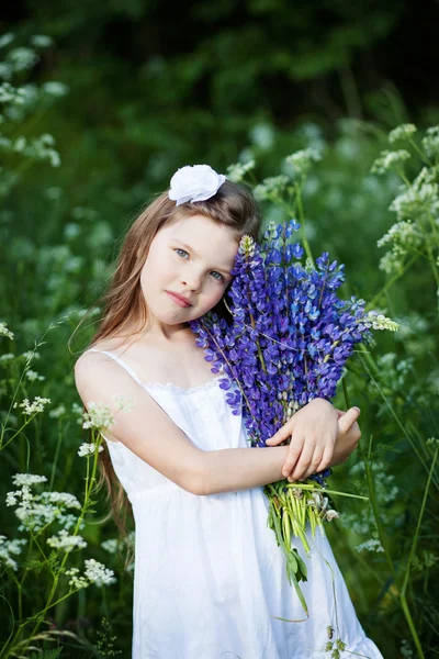 Schöne kleine Mädchen mit lila Lupinen im Freien lizenzfreie Stockbilder