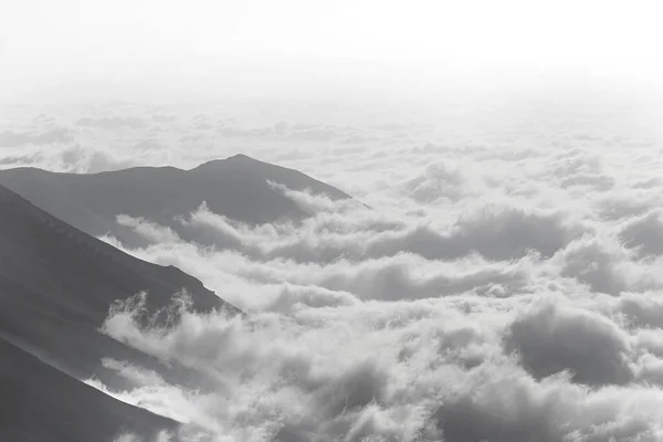 Fog creeping up on mountains, in black and white.