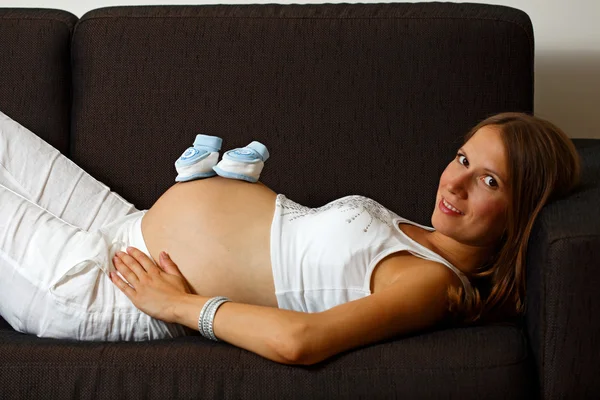 Jeune femme enceinte avec des bottines de bébé sur le ventre — Photo