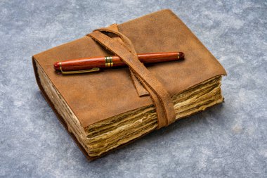 antique leatherbound journal with decked edge handmade paper pages and a stylish pen on a handmade bark paper, journaling concept clipart