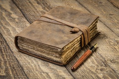 antique leatherbound journal with decked edge handmade paper pages and a stylish pen on a rustic wooden table, journaling concept clipart