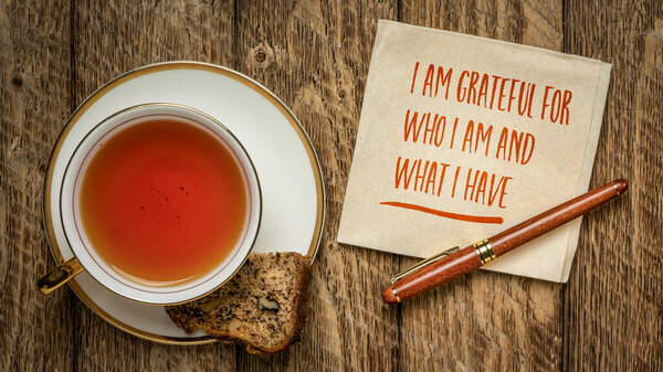 I am grateful for who I am and what I have - inspirational handwriting on a napkin with a cup of tea and banana bread, Thanksgiving concept