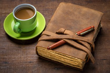 antique leather-bound journal with decked edge handmade paper pages and a stylish pen on a rustic wooden table with a cup of coffee, journaling concept clipart
