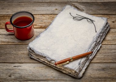 Gri tonlu ağır sıklet kağıt çarşaflı, şık bir kalemle eskiz kitabı ve eski usul ahşaba karşı bir fincan çay.