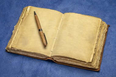 Süslü el yapımı kağıt sayfaları olan boş, antika, deri ciltli bir günlük. Mavi el yapımı kağıda karşı şık bir kalem, günlük kavramı.