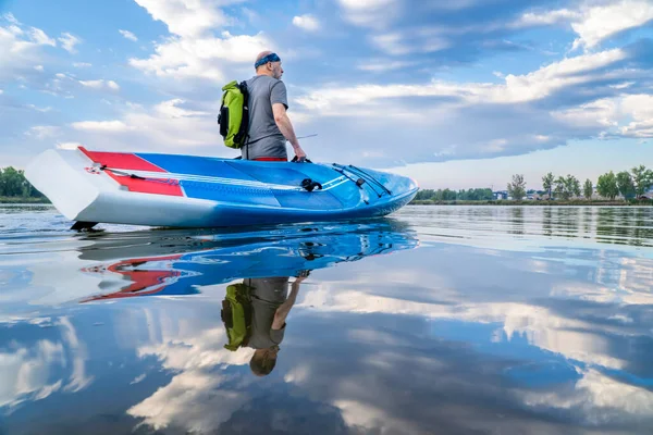 シニア男性スタンドアップ パドラーがコロラド州北部の朝のワークアウトのために湖に彼のレース用パドルボードを起動しています — ストック写真