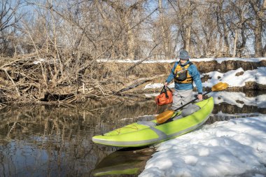 Yaşlı erkek kürekçi, Fort Collins, Colorado 'daki Poudre Nehri' nde kış veya ilkbahar manzaralı küçük bir nehre şişme su kayağı fırlatıyor.