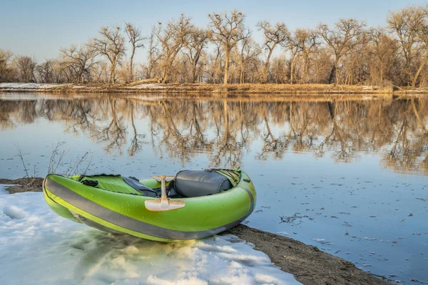 inflatable whitewater kayak on a lake shore with blue heron rookery in background, Fort Collins, Colorado, winter or early spring scenery