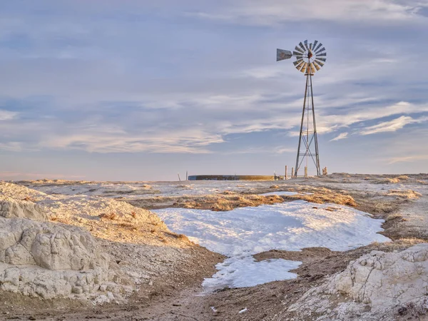 windmill with a pump and cattle water tank in shortgrass prairie, Pawnee National Grassland in northern Colorado, winter or early spring scenery