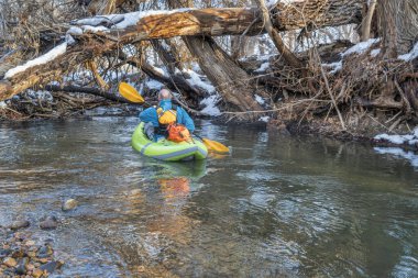 Son sınıf öğrencisi erkek, Fort Collins, Colorado 'daki Poudre Nehri' nde, kış veya ilkbahar manzarasında şişme beyaz su kayağında kürek çekiyor.