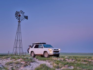 Grover, CO, USA - July 7, 2021: Toyota 4Runner SUV (2016 Trail edition) before sunrise in Pawnee National Grassland in northern Colorado, summer scenery with a windmill and cattle water tank.