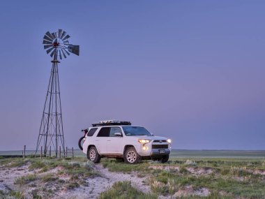 Grover, CO, USA - July 7, 2021: Toyota 4Runner SUV (2016 Trail edition) before sunrise in Pawnee National Grassland in northern Colorado, summer scenery with a windmill and cattle water tank. clipart