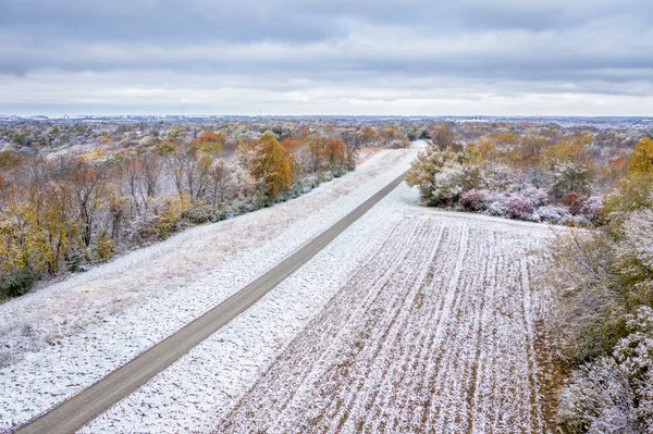Gravel road, forest and harvested corn field dusted by early snow, aerial view of Honey Creek Conservation Area in western Missouri