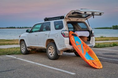 Boyd Lake State Park, CO, USA - July 27, 2021 : A prone kayak by Bellyak id being loaded into Toyota 4 Runner SUV on a lake shore at dusk after paddling session. clipart