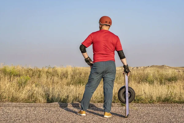 mature senior male with one-wheeled electric skateboard on a prairie road, late summer scenery with haze and smoke from distant wildfires