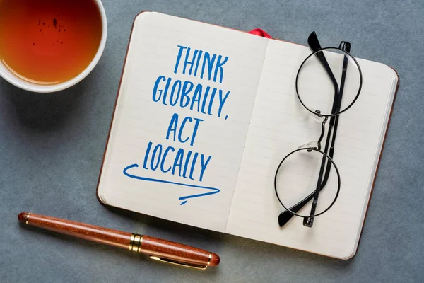 Think globally, act locally reminder - handwriting in a notebook or journal with a cup of tea, business, education and environment concept