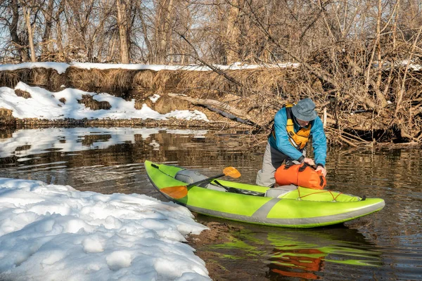シニア男性のパドラーが小さな川で膨脹可能なホワイトウォーターカヤックを起動しています フォートコリンズ コロラド州 冬または早春の風景 — ストック写真