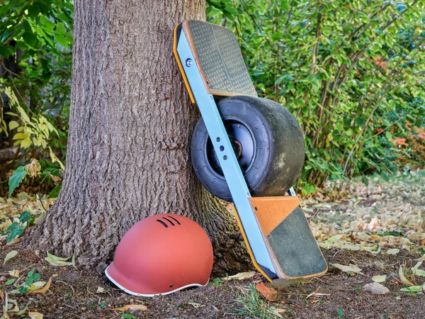 one-wheeled electric skateboard with a helmet in a park in fall scenery