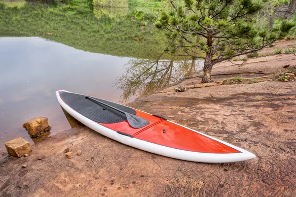 Ayağa kalkıp bir kayalık göl kıyısında paddleborad — Stok fotoğraf