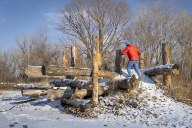 Yürüyüş direkleri olan yürüyüşçü, Fort Collins, Colorado 'daki Poudre nehrinin kıyısında, soğuk kış manzarasında erozyon kontrol yapısına tırmanıyor.