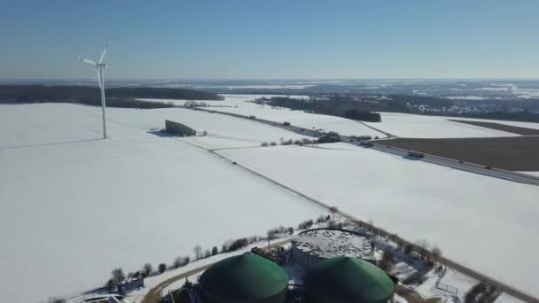 Luftaufnahme von Biogasanlage und Windkraftanlage im ländlichen Deutschland bei Winterschnee an einem sonnigen Tag mit strahlend blauem Himmel — Stockvideo