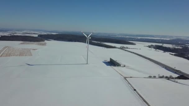 독일 남부 울름 근처 고속 도로 A8 근처의 눈덮인 풍력 터빈의 공중 사진, 맑은 겨울 날씨에 푸른 하늘과 눈 위에 보이는 그림자 — 비디오