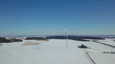 Güney Almanya 'da Ulm yakınlarındaki A8 karayolunun yanındaki karla kaplı rüzgar türbininin hava görüntüsü güneşli bir kış gününde büyük mavi gökyüzü ve karların üzerinde görünen bir gölgeyle