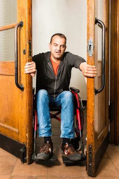 Homem em cadeira de rodas preso entre portas de balanço — Fotografia de Stock