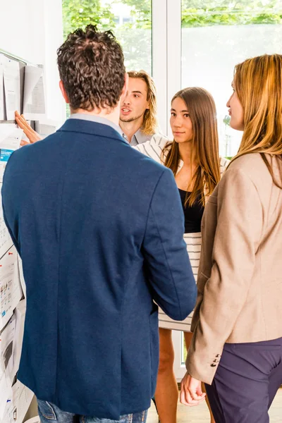 Businesspeople looking at bulletin board in office — Stock Photo, Image