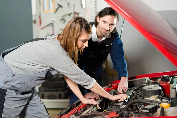 Auto mechanic guiding a female trainee in garage Royalty Free Stock Photos