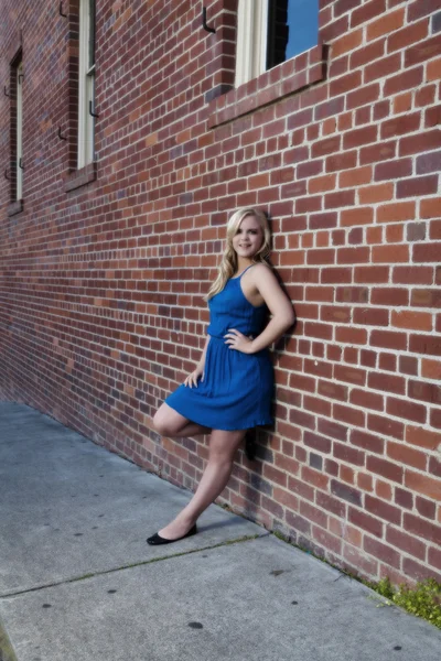 Mulher loira em vestido azul inclinado na parede de tijolo — Fotografia de Stock