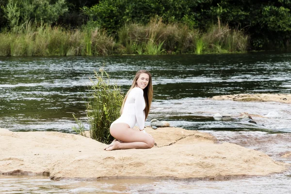 Kir nehir üzerinde oturan beyaz Teen kadın beyaz tek parça streç giysi — Stok fotoğraf