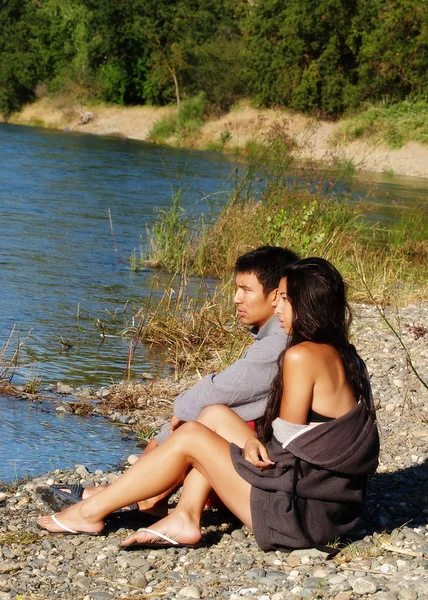Casal étnico sentado ao ar livre na margem do rio — Fotografia de Stock