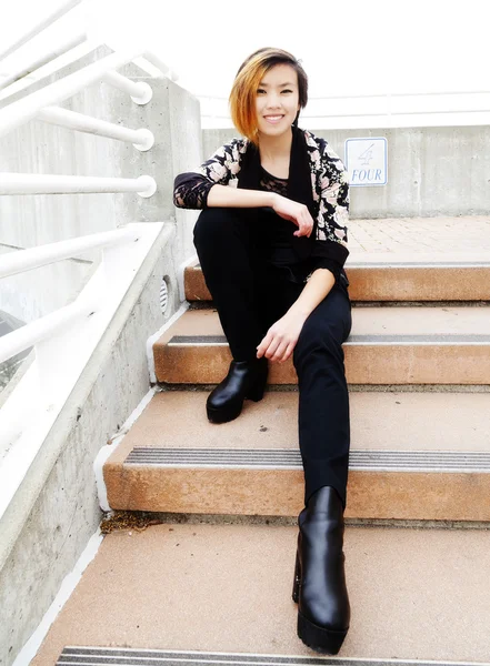 Улыбающаяся американка азиатского происхождения сидит на ступеньках — стоковое фото